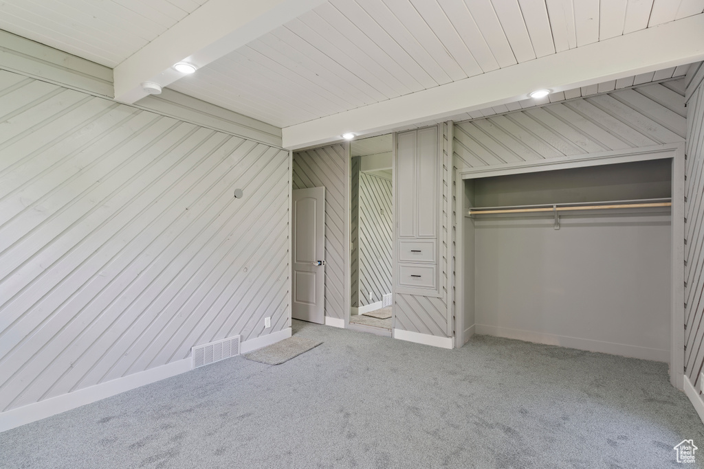 Unfurnished bedroom with carpet, a closet, baseboards, wooden ceiling with exposed beams, and wood walls