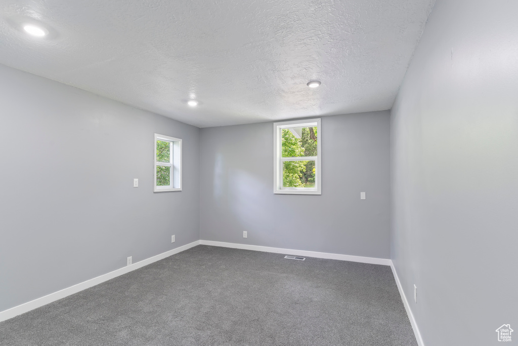 Unfurnished room featuring a textured ceiling, baseboards, dark carpet, and recessed lighting