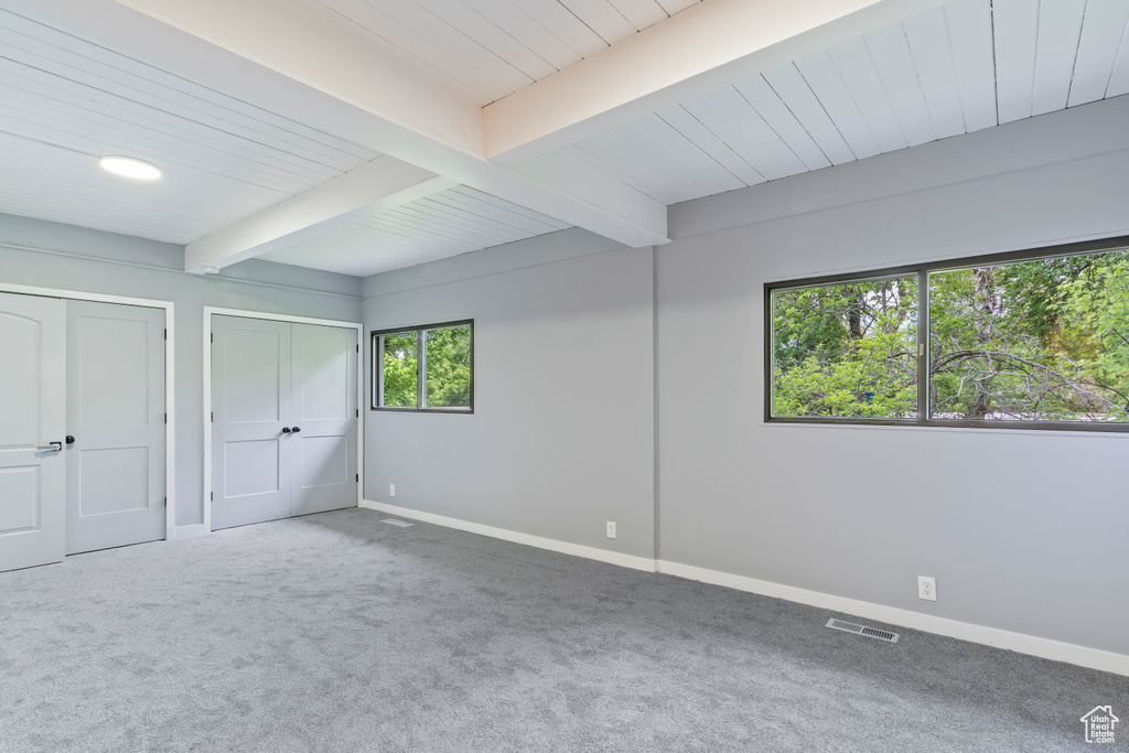 Unfurnished bedroom with beamed ceiling, carpet floors, baseboards, and two closets