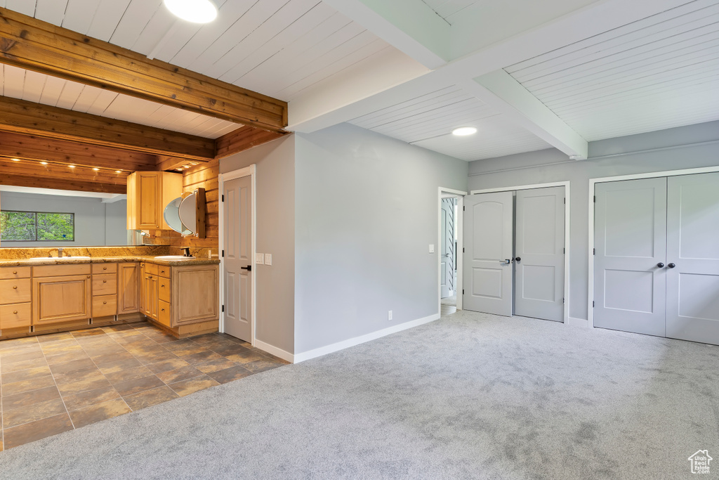 Kitchen featuring carpet, beam ceiling, light brown cabinetry, baseboards, and a sink