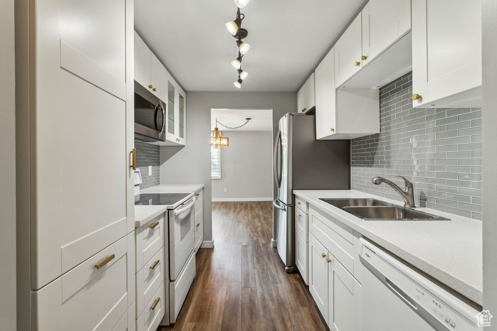 Kitchen with white appliances, a sink, backsplash, dark wood-type flooring, and white cabinets