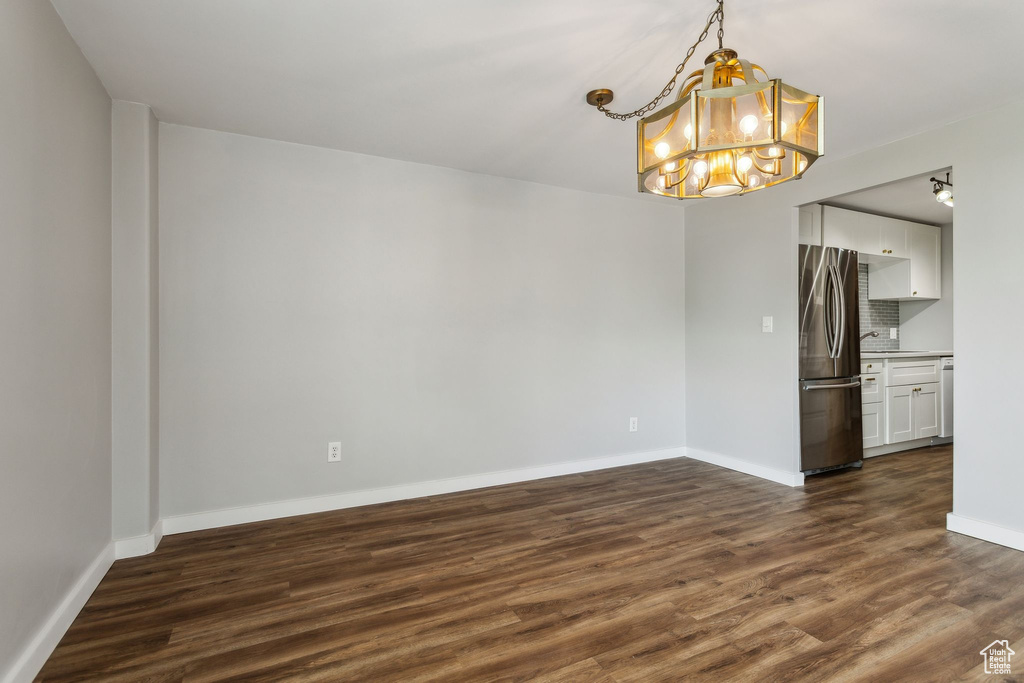 Spare room with a chandelier, dark wood-style floors, baseboards, and a sink