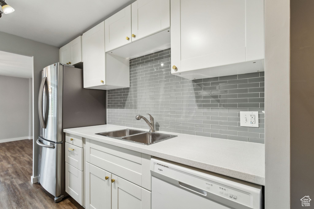 Kitchen with white dishwasher, a sink, white cabinetry, backsplash, and light countertops