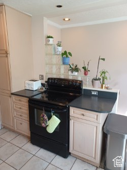 Kitchen with black range with electric cooktop, light tile patterned flooring, dark countertops, and recessed lighting