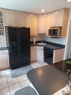 Kitchen with black appliances, a sink, dark countertops, light tile patterned flooring, and recessed lighting