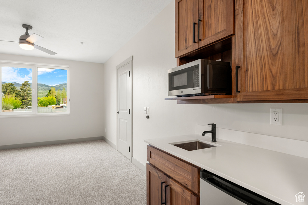 Kitchen featuring stainless steel microwave, a sink, light carpet, and brown cabinets