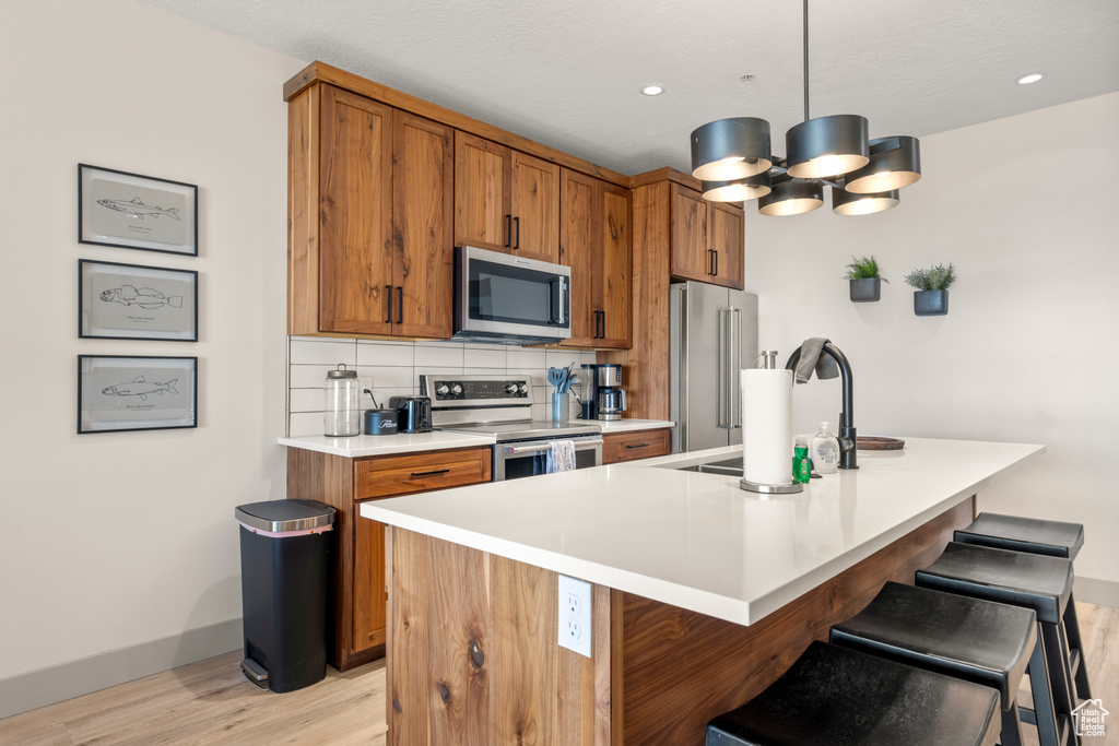 Kitchen with stainless steel appliances, light wood-style floors, brown cabinets, a sink, and recessed lighting