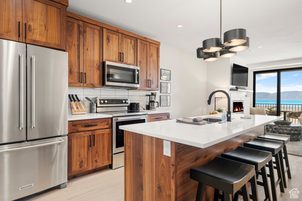 Kitchen featuring appliances with stainless steel finishes, brown cabinets, a sink, light countertops, and open floor plan