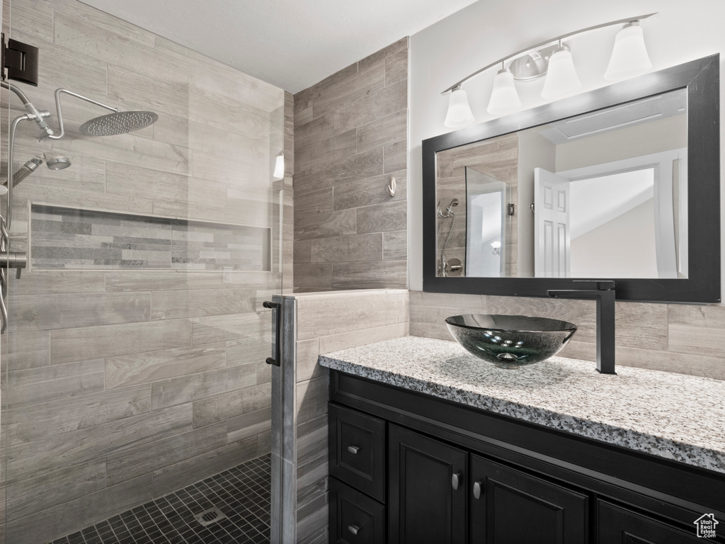 Bathroom featuring a stall shower, vanity, tile walls, and backsplash