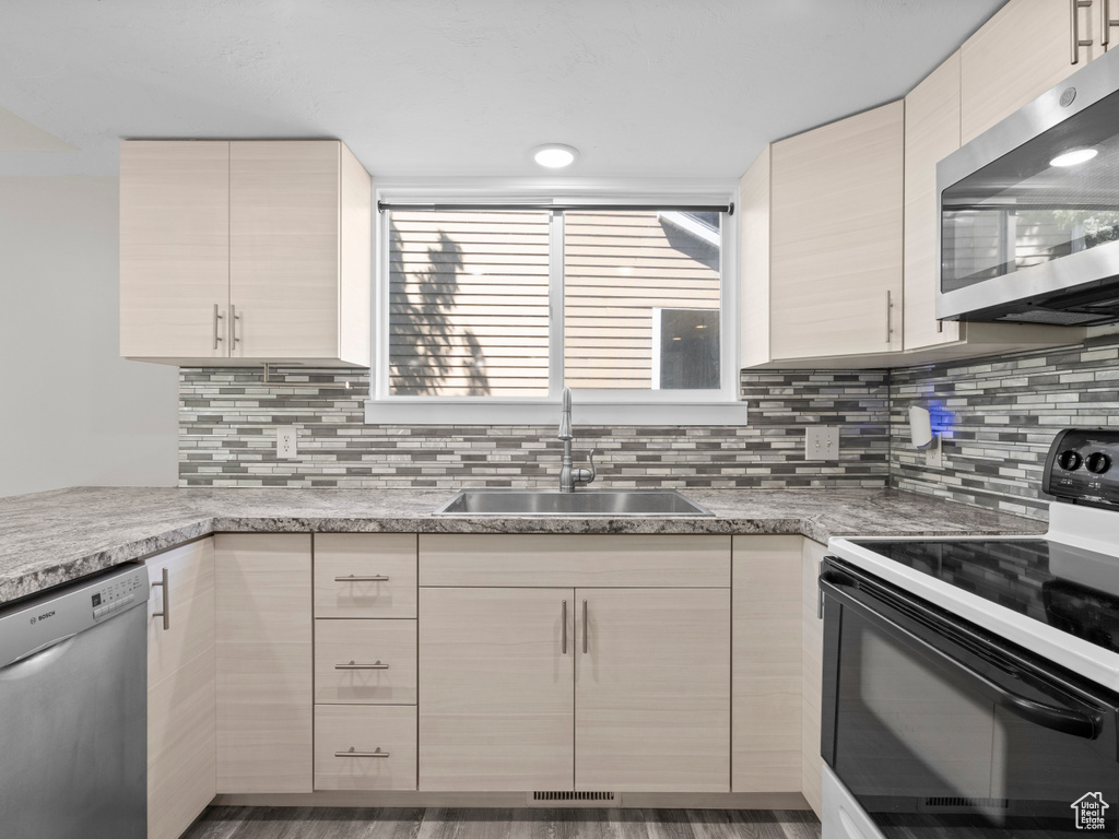 Kitchen with appliances with stainless steel finishes, a sink, light countertops, and backsplash