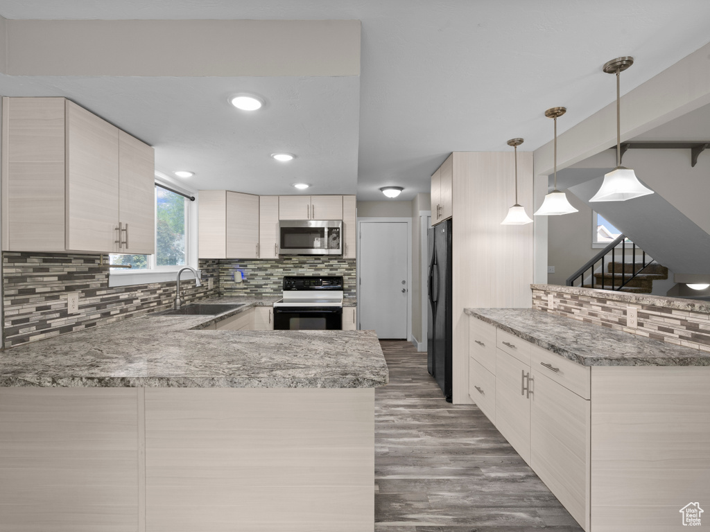 Kitchen with black appliances, a sink, a peninsula, tasteful backsplash, and wood finished floors