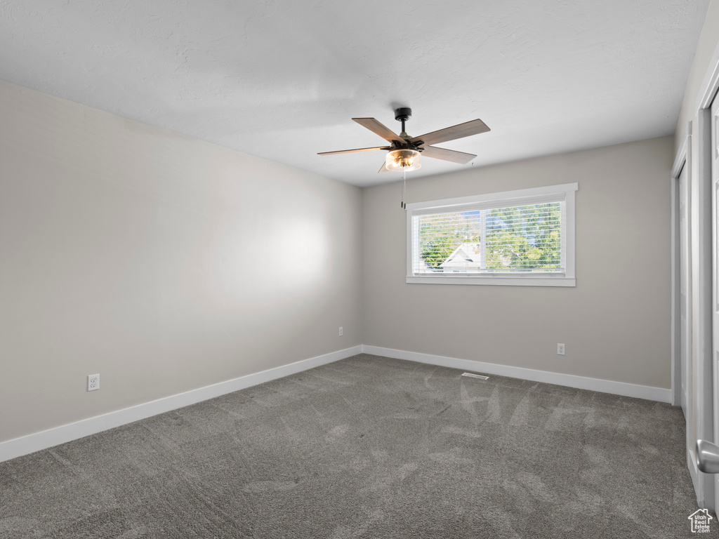 Unfurnished bedroom featuring dark colored carpet, baseboards, and a ceiling fan