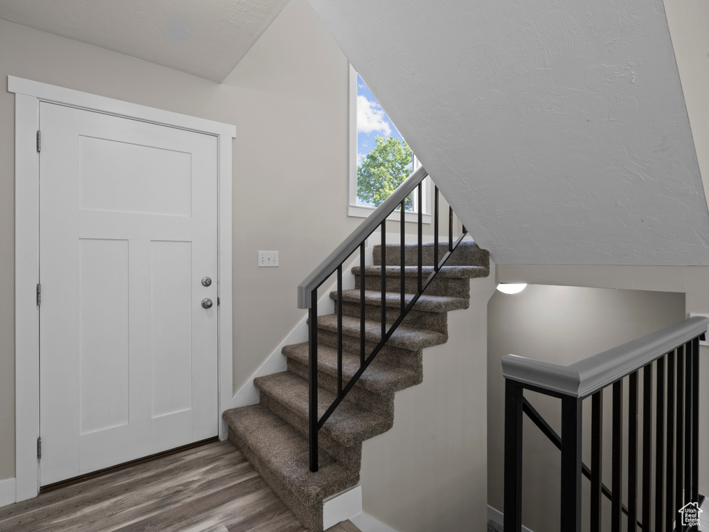 Stairs with wood finished floors, baseboards, and vaulted ceiling