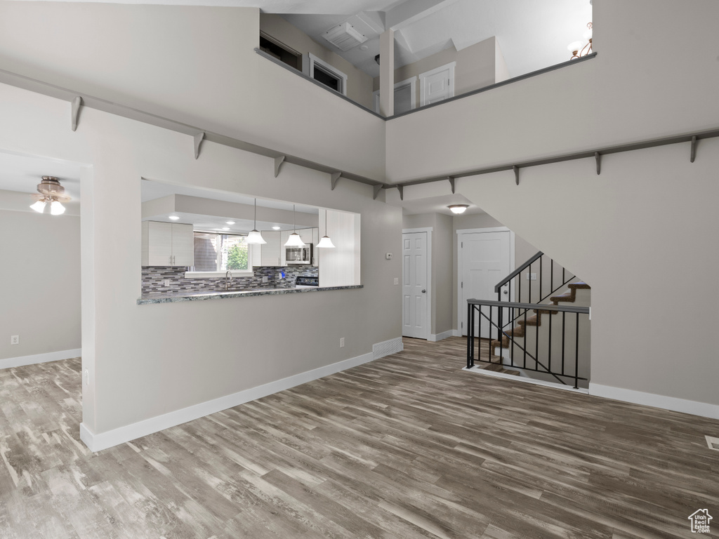 Spare room with wood finished floors, baseboards, stairway, a high ceiling, and ceiling fan