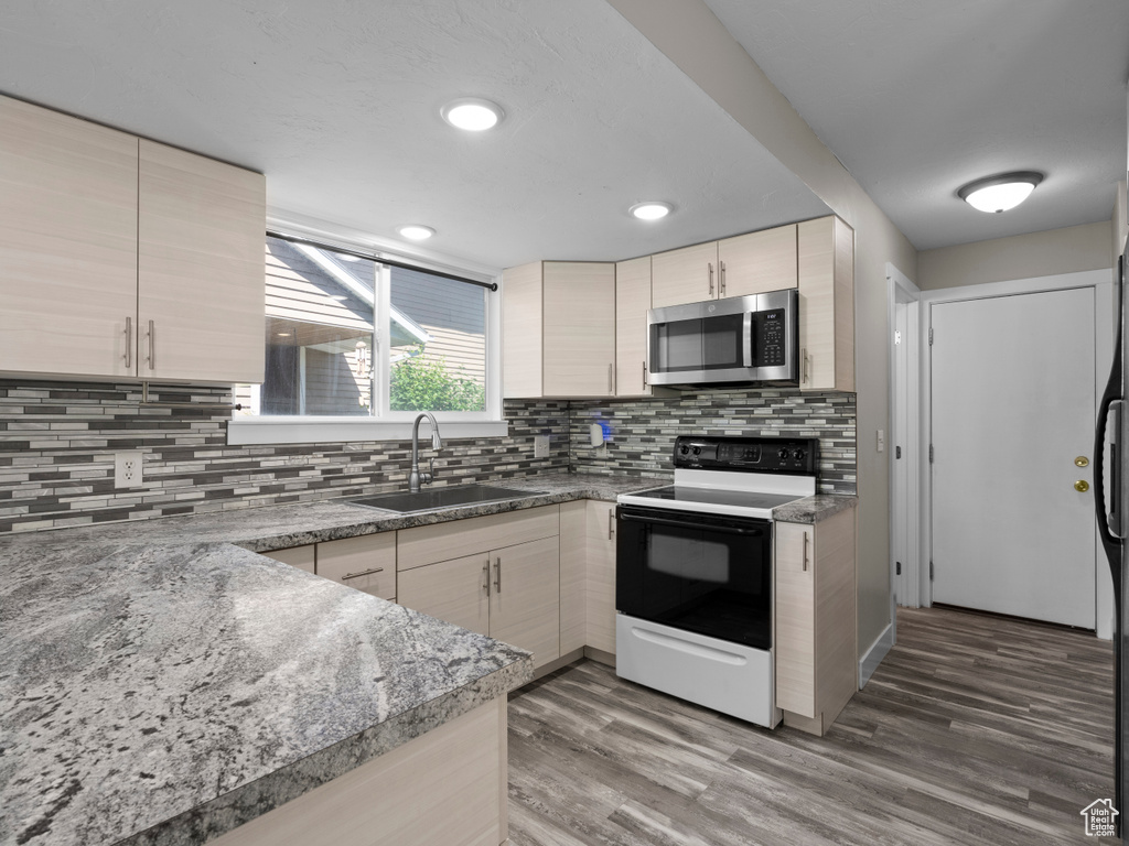 Kitchen featuring stainless steel microwave, a sink, range with electric stovetop, backsplash, and light wood finished floors