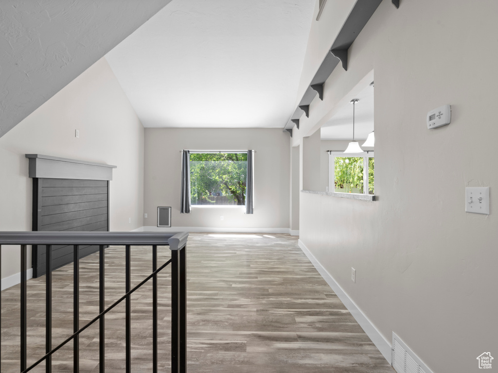 Hall with baseboards, wood finished floors, plenty of natural light, and vaulted ceiling