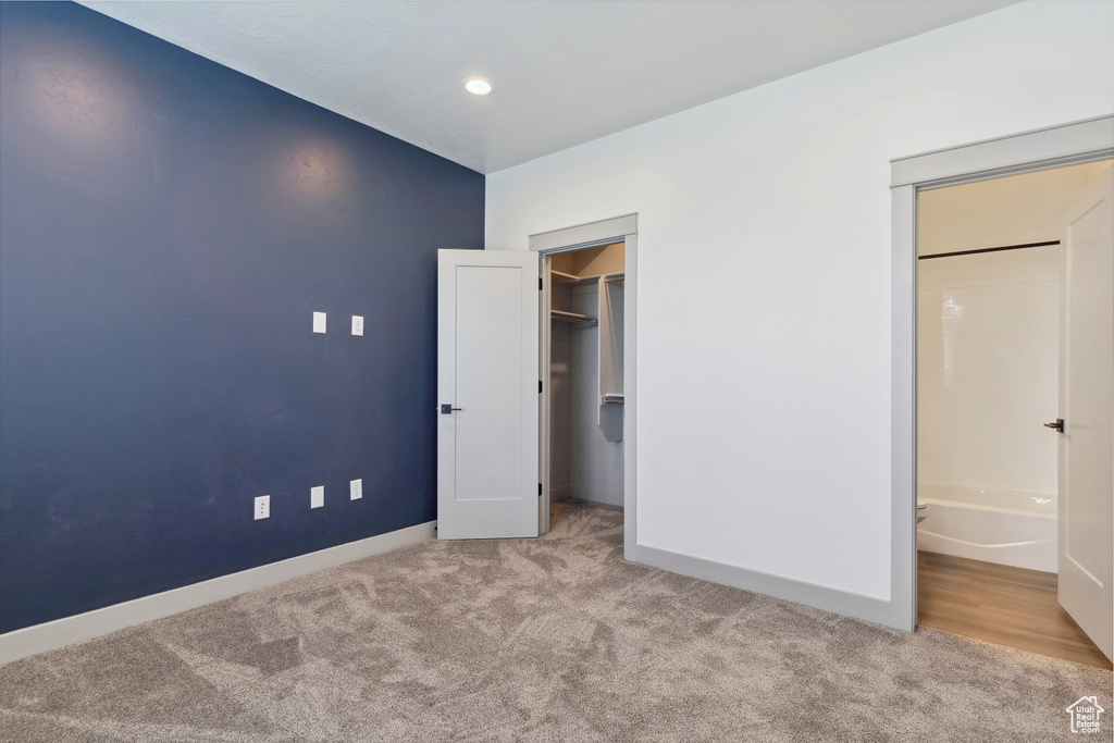 Unfurnished bedroom featuring carpet flooring, baseboards, a spacious closet, recessed lighting, and ensuite bath