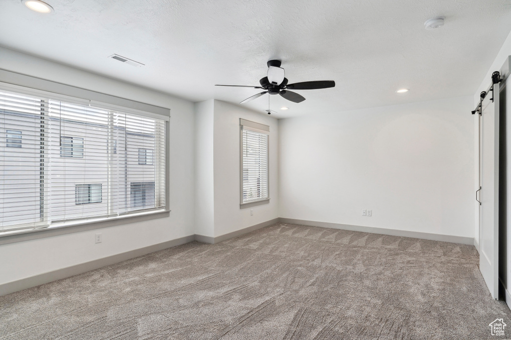 Empty room featuring a barn door, light carpet, ceiling fan, a smoke detector, and recessed lighting