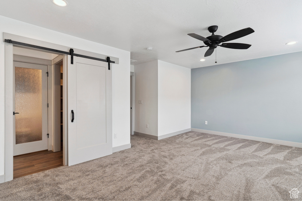 Unfurnished bedroom with carpet flooring, a barn door, recessed lighting, baseboards, and ceiling fan