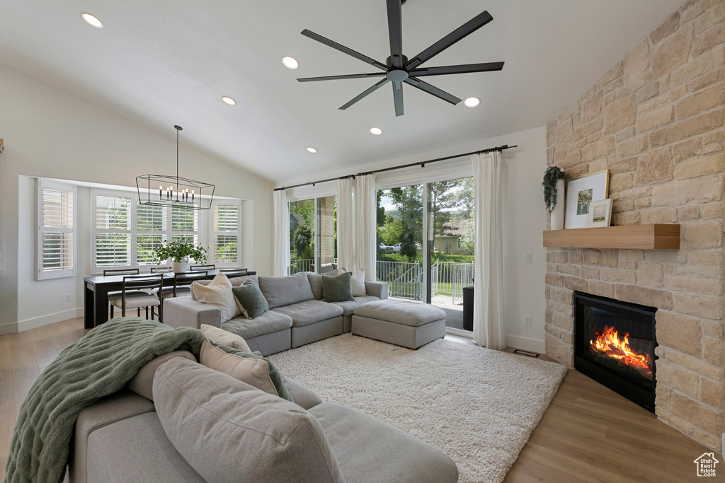 Living area with vaulted ceiling, a chandelier, recessed lighting, light wood finished floors, and a stone fireplace