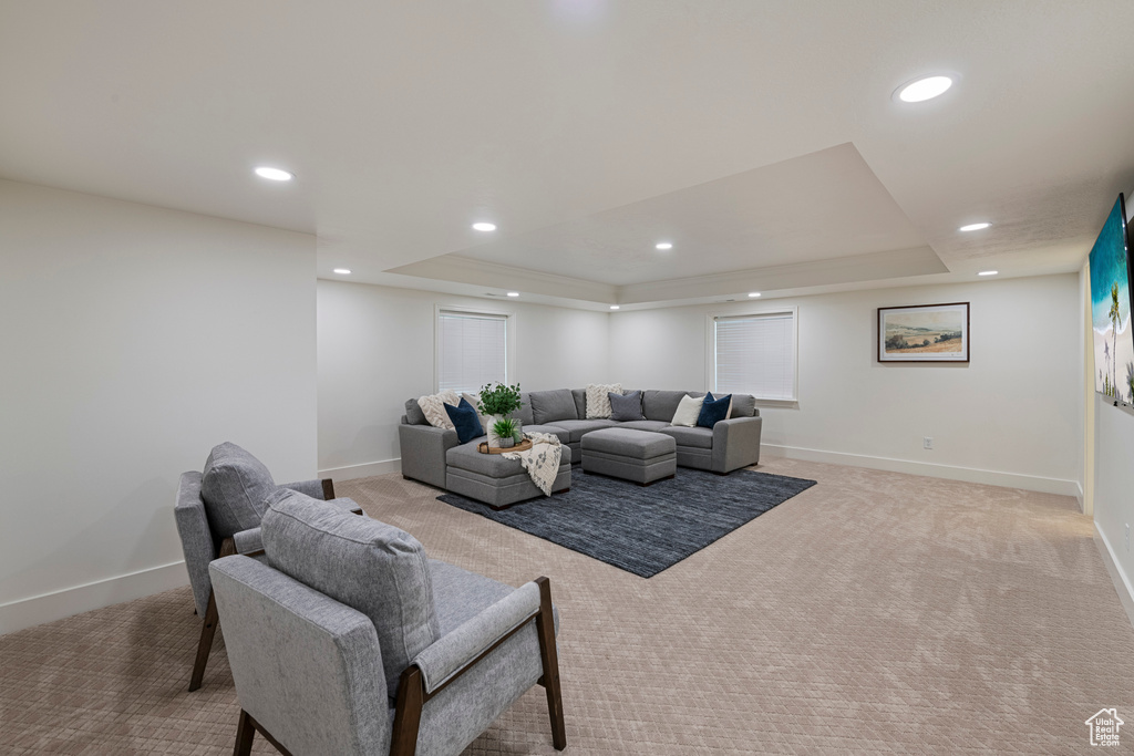 Living room with light colored carpet, a raised ceiling, baseboards, and recessed lighting