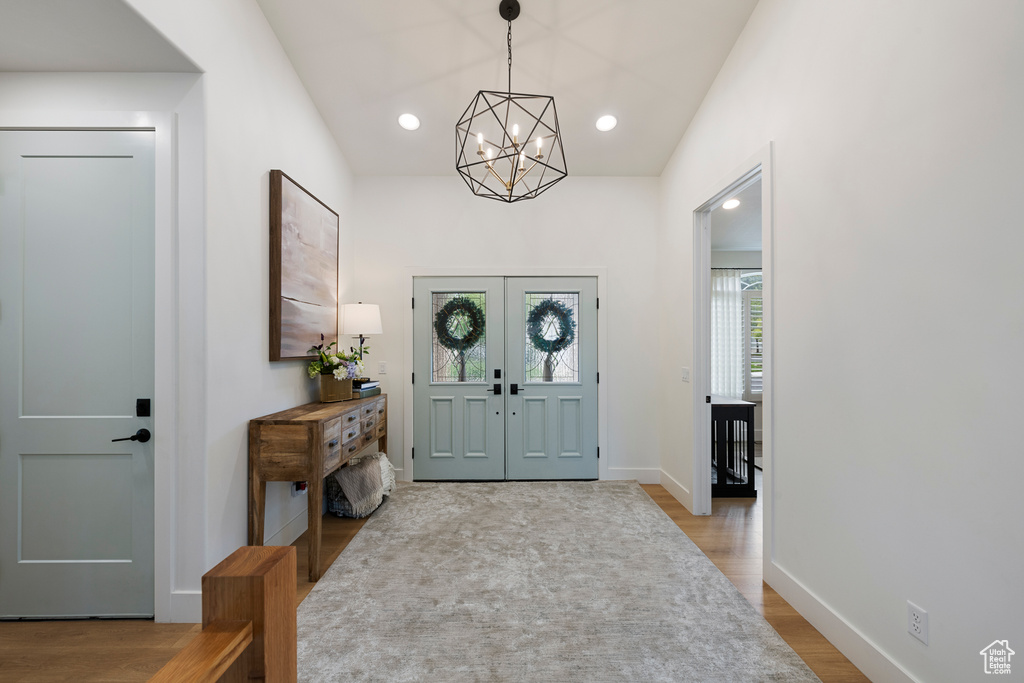 Foyer entrance with a chandelier, wood finished floors, baseboards, vaulted ceiling, and french doors