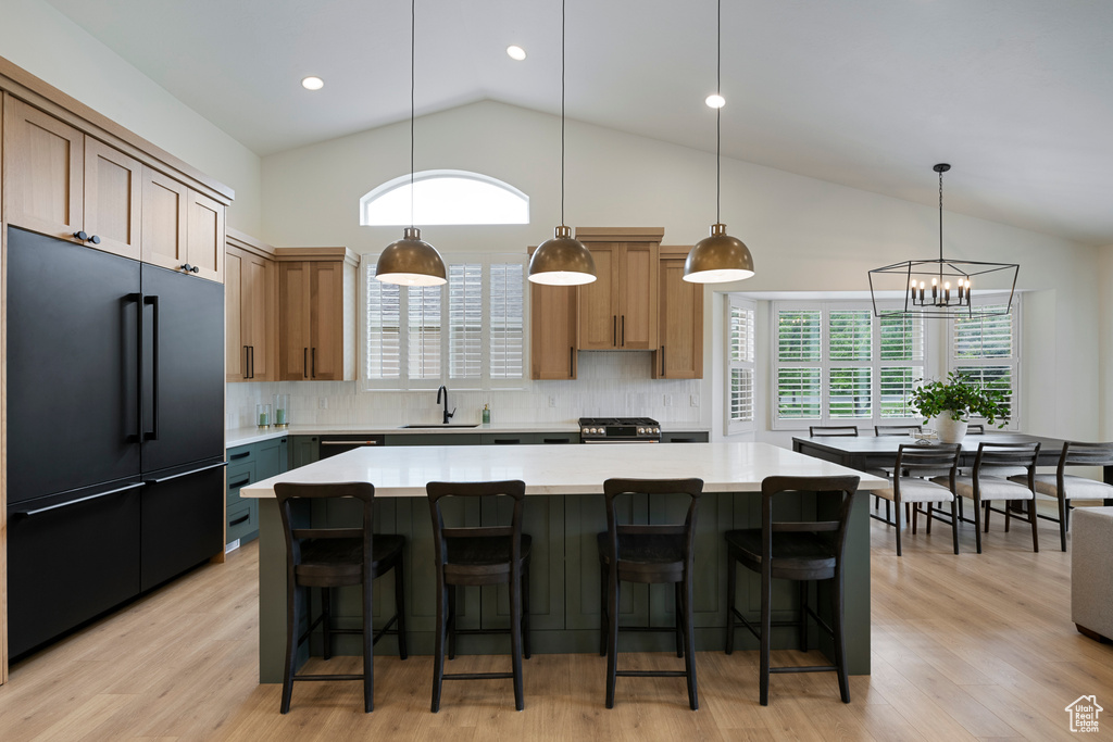 Kitchen with high end black fridge, backsplash, light countertops, a sink, and high vaulted ceiling