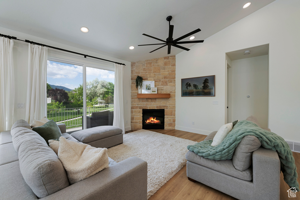 Living room featuring vaulted ceiling, a ceiling fan, wood finished floors, recessed lighting, and a stone fireplace