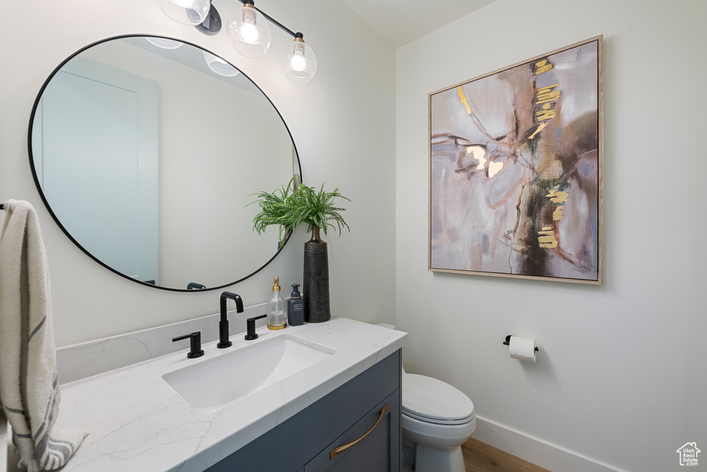 Bathroom with toilet, vanity, wood finished floors, and baseboards
