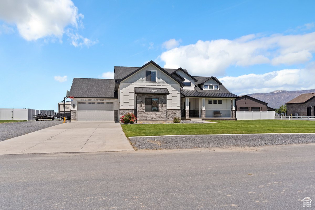 Modern farmhouse style home with a standing seam roof, stone siding, an attached garage, concrete driveway, and metal roof