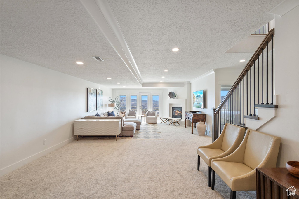Living room featuring a textured ceiling, light carpet, recessed lighting, stairs, and a glass covered fireplace