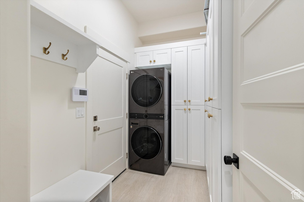 Laundry room featuring stacked washer / drying machine, cabinet space, and light wood finished floors