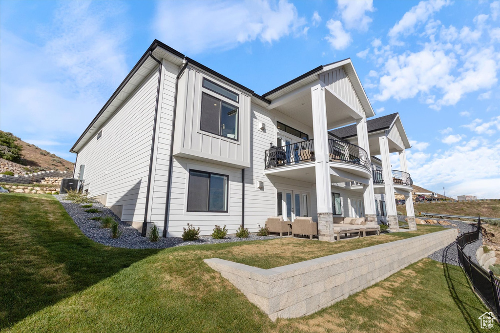 Back of property with a balcony, outdoor lounge area, a yard, board and batten siding, and a patio