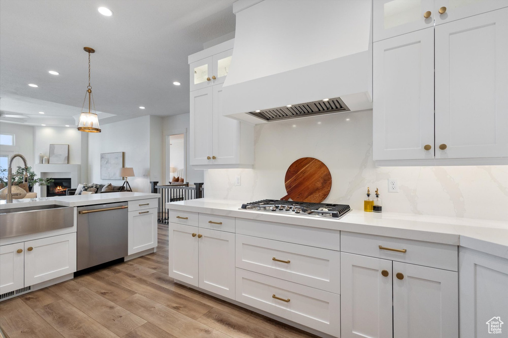 Kitchen with stainless steel appliances, custom exhaust hood, white cabinetry, recessed lighting, and a sink
