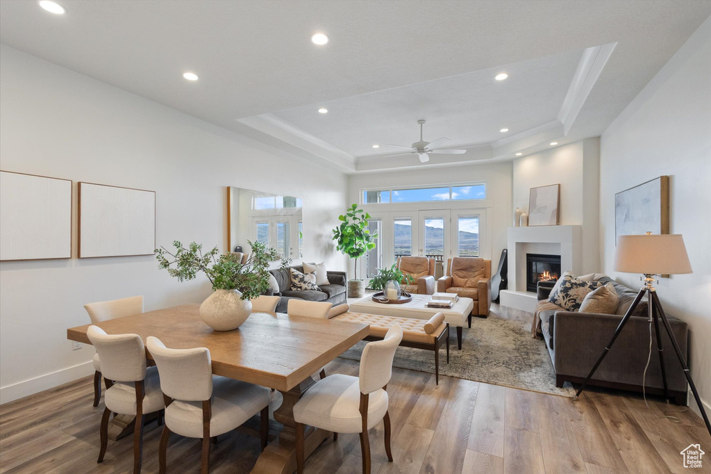Dining area featuring a raised ceiling, light wood finished floors, a ceiling fan, recessed lighting, and a glass covered fireplace