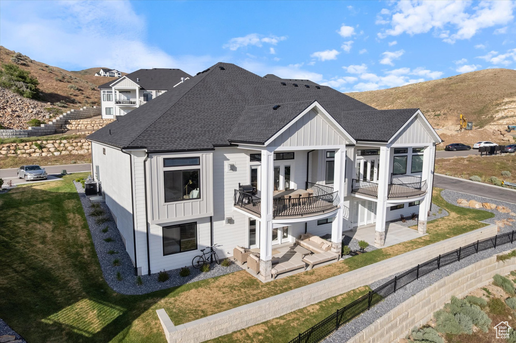 Back of house with a shingled roof, a patio, a balcony, a mountain view, and board and batten siding