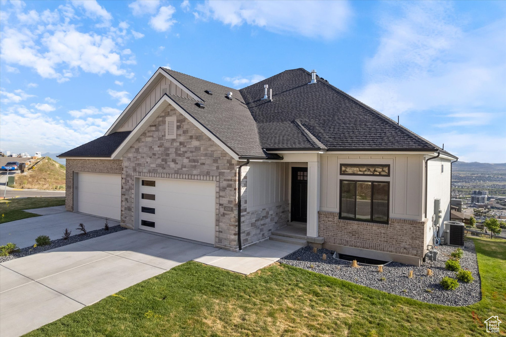 View of front of property featuring board and batten siding, an attached garage, driveway, a front yard, and central AC unit