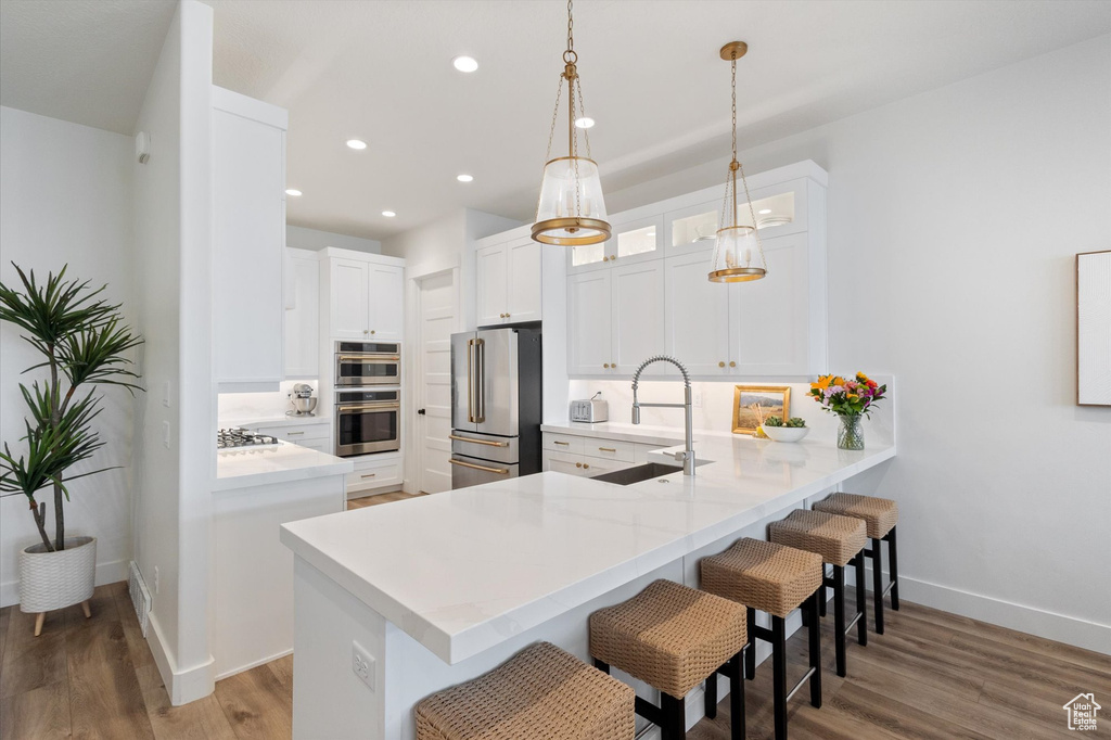 Kitchen with appliances with stainless steel finishes, a sink, a peninsula, a kitchen bar, and light countertops