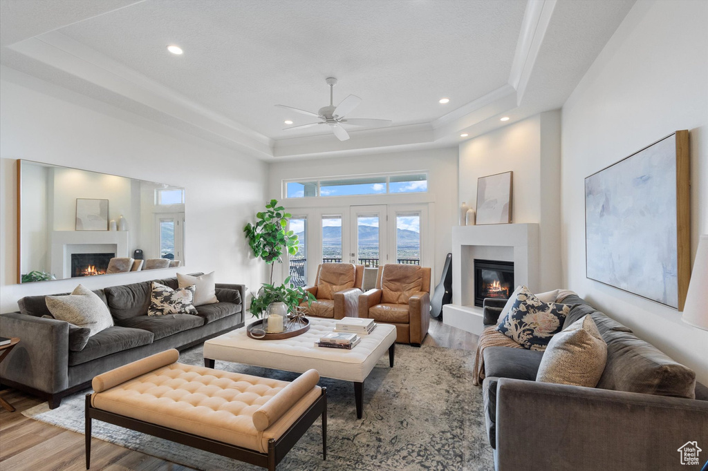 Living room featuring a glass covered fireplace, a raised ceiling, light wood finished floors, a ceiling fan, and recessed lighting