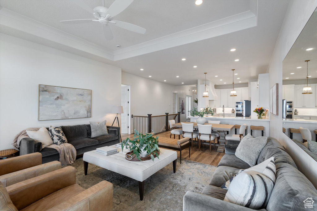 Living room featuring light wood finished floors, recessed lighting, a ceiling fan, crown molding, and a raised ceiling