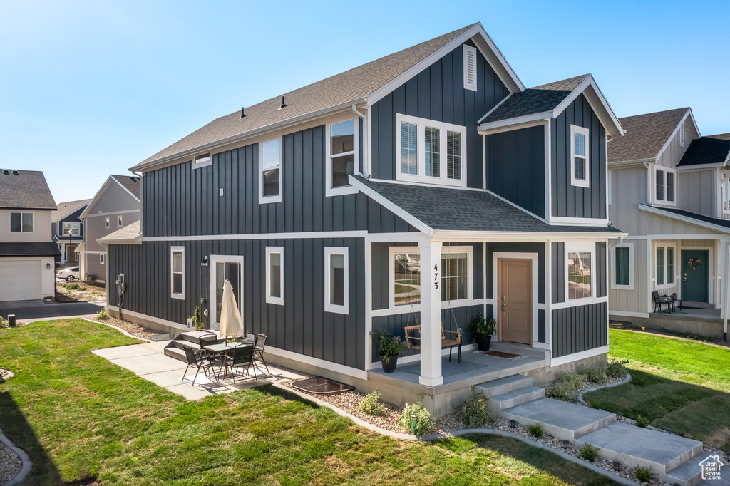 Back of house featuring a lawn, a shingled roof, board and batten siding, and a patio area