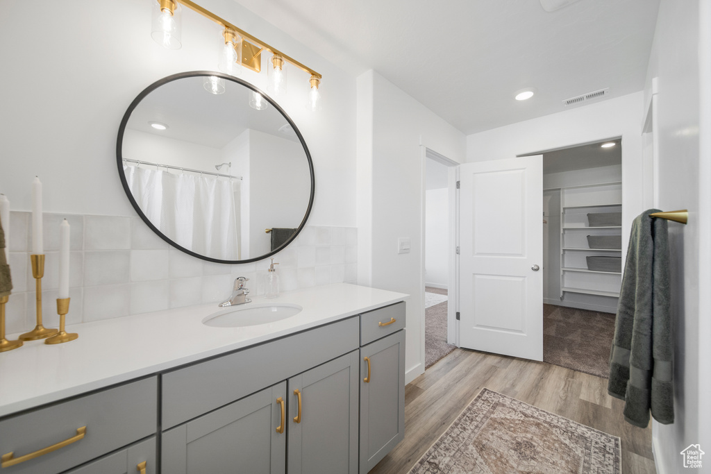 Full bath with visible vents, vanity, wood finished floors, recessed lighting, and backsplash