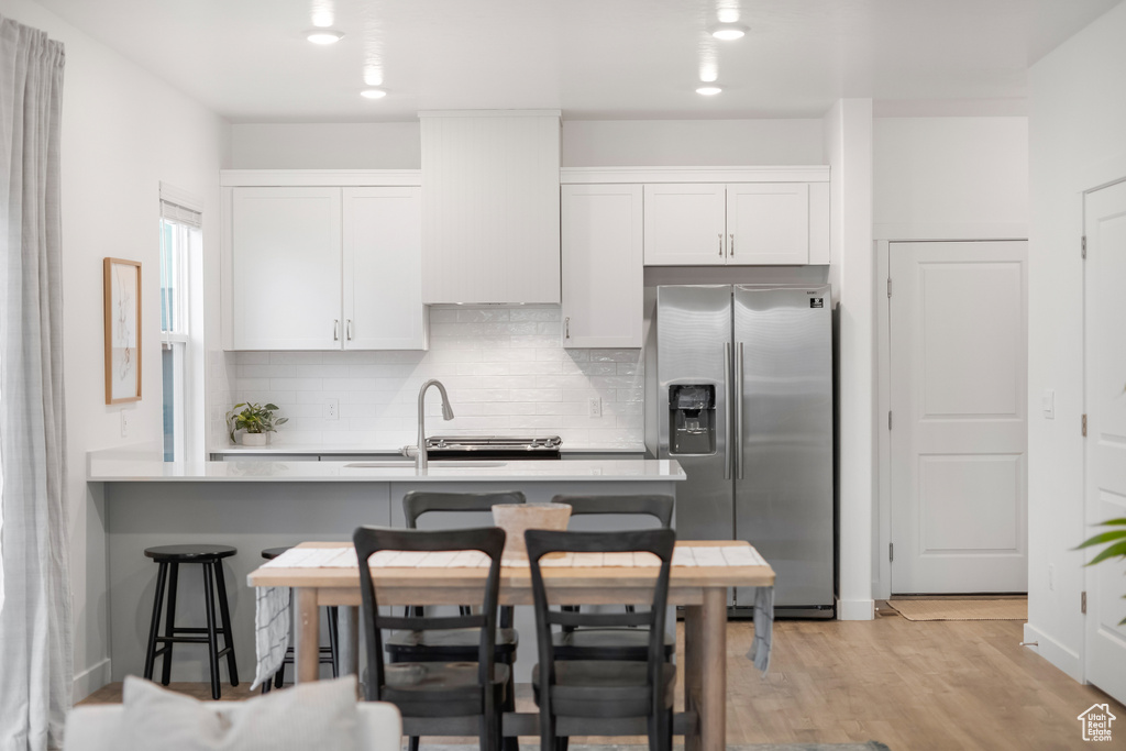 Kitchen with decorative backsplash, a kitchen bar, a sink, white cabinets, and stainless steel fridge