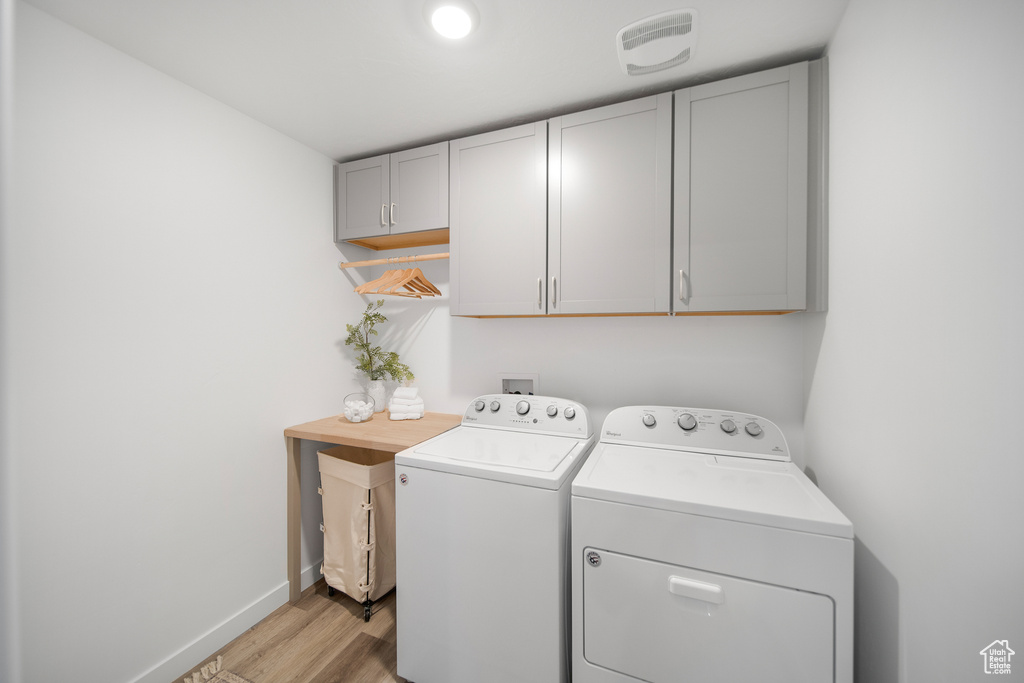 Clothes washing area with independent washer and dryer, visible vents, cabinet space, baseboards, and light wood finished floors