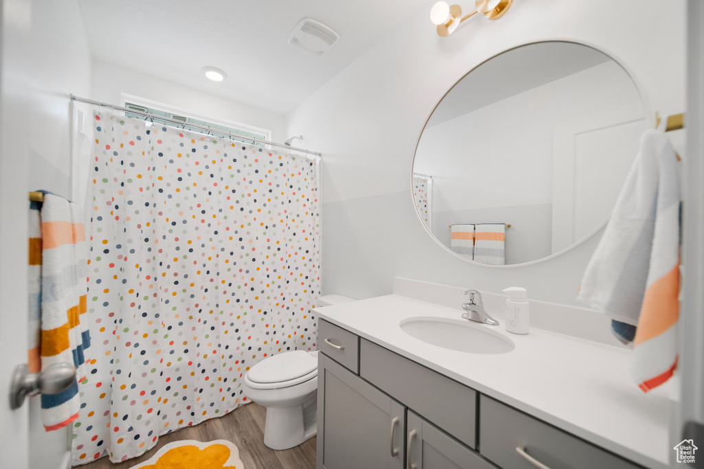 Bathroom featuring a shower with curtain, visible vents, wood finished floors, vanity, and toilet