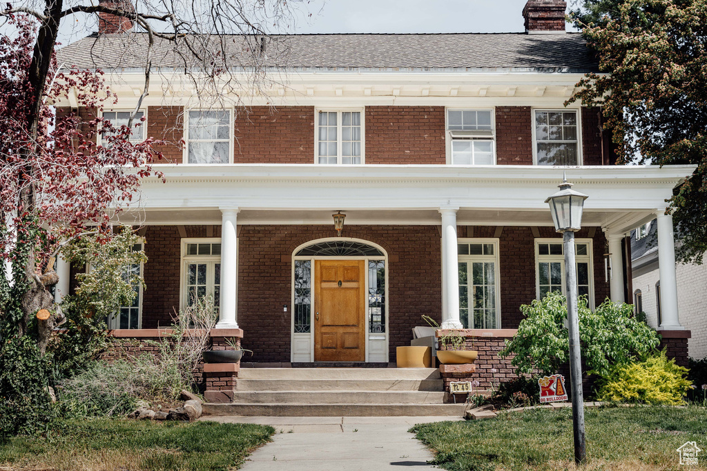 View of front of home featuring a chimney, a porch, and brick siding