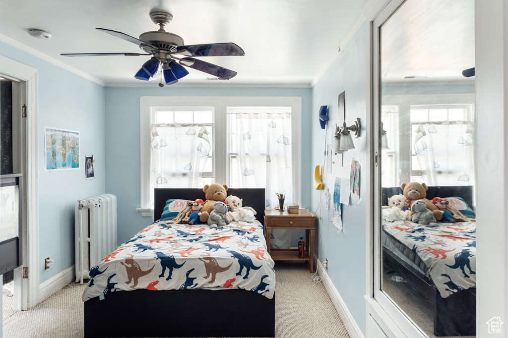 Bedroom with radiator, light colored carpet, baseboards, ornamental molding, and a ceiling fan