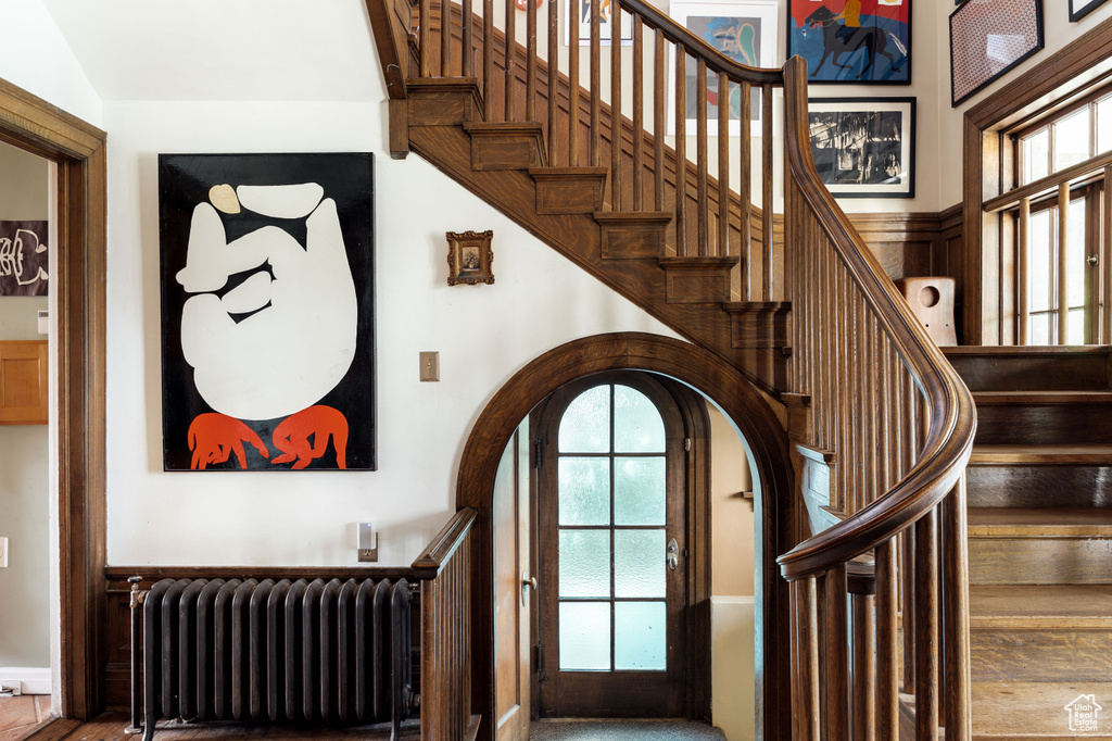 Foyer featuring radiator, arched walkways, stairway, and a high ceiling