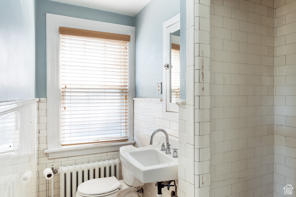 Half bath featuring radiator, tile walls, a sink, toilet, and wainscoting