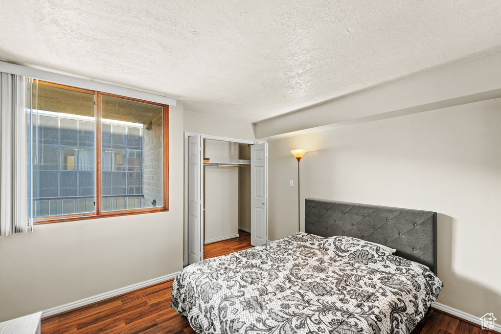 Bedroom featuring dark wood finished floors, a closet, a textured ceiling, and baseboards